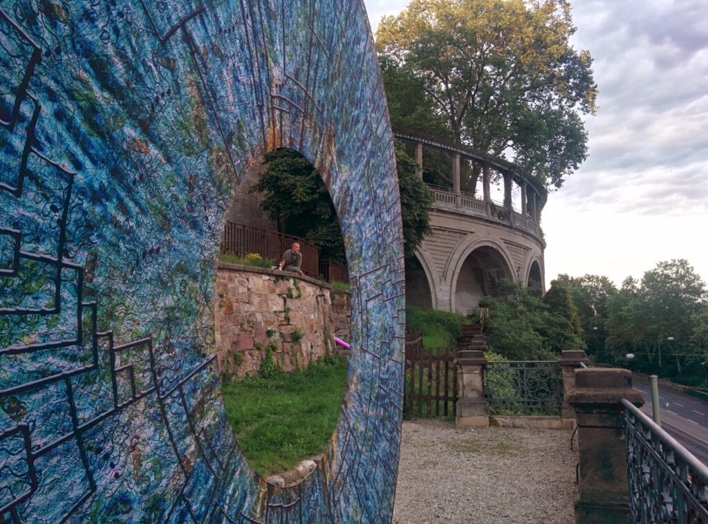 IRIDO, LICHT(e)WEGE in Kassel, 2014: Ring aus blauem Geflecht vor Bäumen und altem Mauerwerk