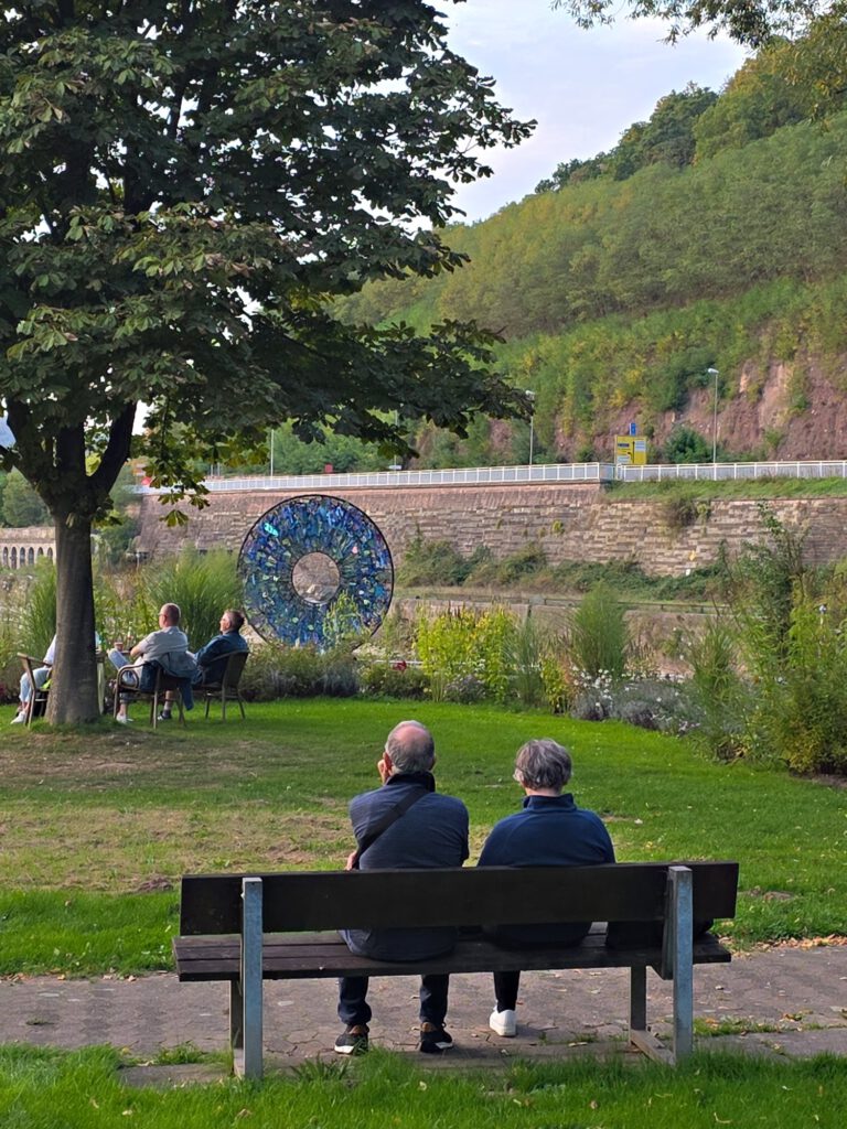 Besucher auf einer Bank im Park, im Hintergrund AIRIS am Fluss