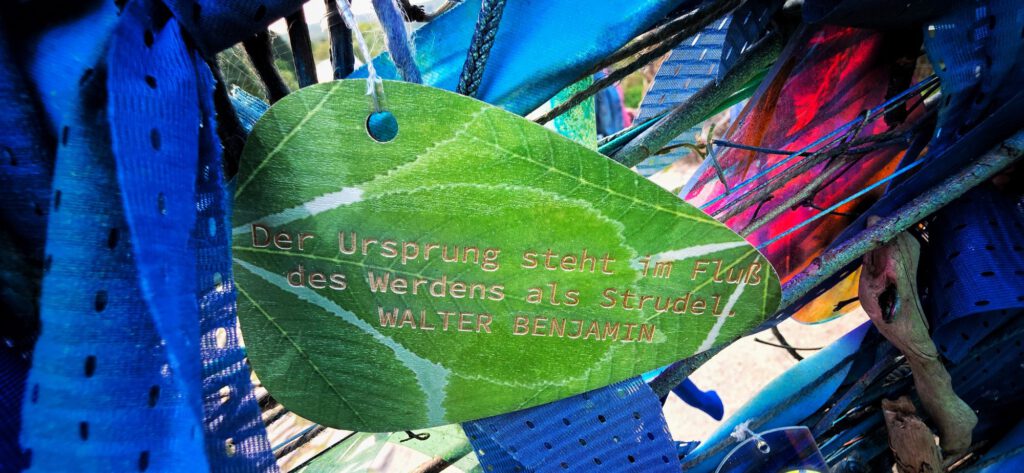 Plakette mit Zitat von Walter Benjamin: Der Ursprung steht im Fluß des Werdens als Strudel.